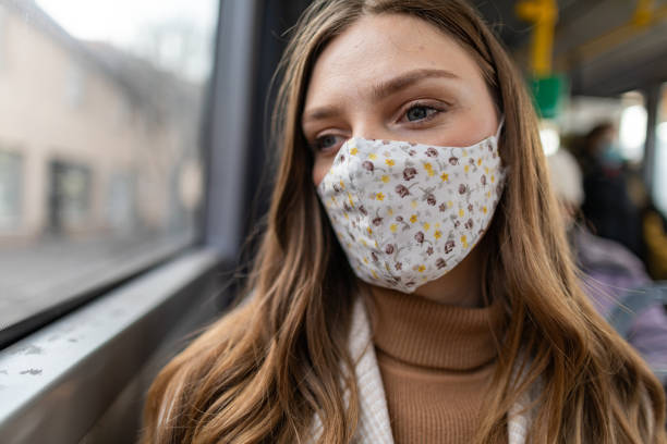 istock Depressed young woman with protective face mask looking through the window while traveling by bus 1300036598