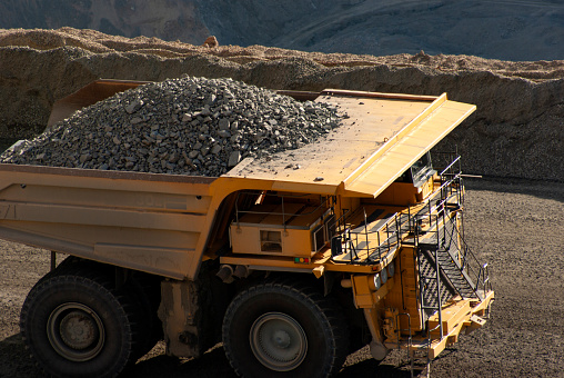 A very large yellow dumptruck in a large mine hauling copper ore.