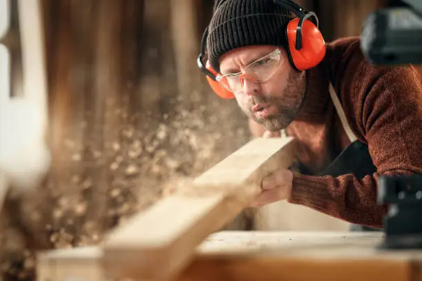 Photo of Carpenter blowing sawdust from wooden plank