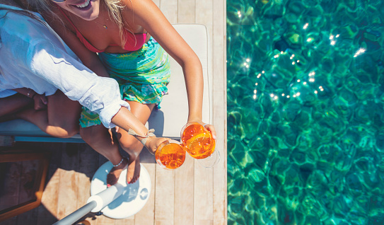 Women  toasting with a spritz cocktail on a deck over the ocean. One of the women is wearing a bikini and is smiling. Turquoise ocean is crystal clear. Copy space