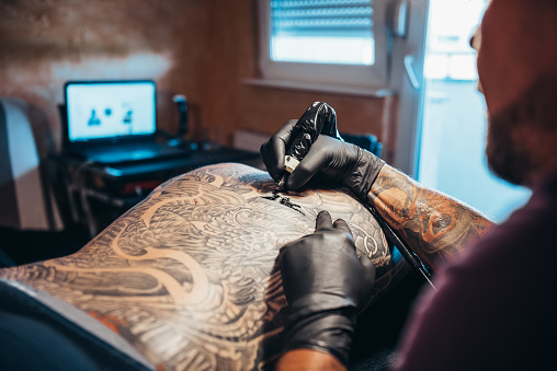 A cropped shot of a tattooed young mans back getting more tattoos