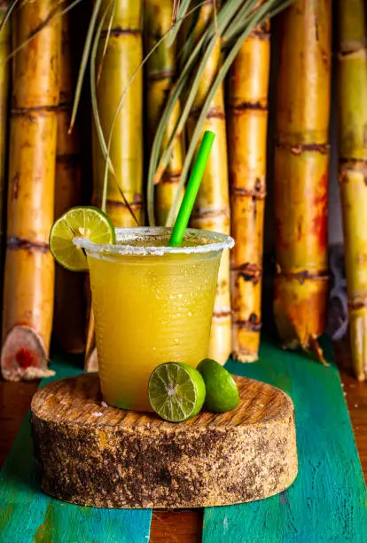 Sugarcane juice in plastic cup with abstract background whit lemon and salt amd plants on background