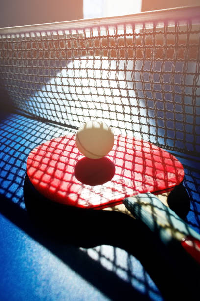 une raquette de tennis de table rouge et une balle blanche se trouvent sur la surface de la table à côté du filet. jeu de sport - table tennis table tennis racket racket sport ball photos et images de collection