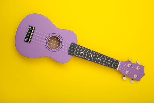 four string ukulele guitar yellow background - plucking an instrument imagens e fotografias de stock