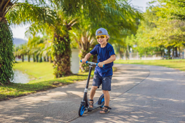 Child on kick scooter in park. Kids learn to skate roller board. Little boy skating on sunny summer day. Outdoor activity for children on safe residential street. Active sport for preschool kid. niño en patinete scooter en el parque. los niños aprenden a patinar en el tablero. pequeño niño patinando en el soleado día de verano. actividad al aire libre para niños en calle residencial segura. deporte activo para niños en edad preescolar