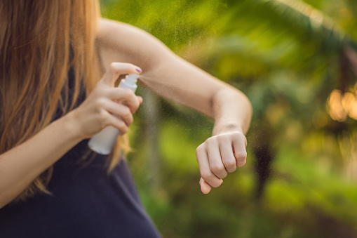 Woman spraying insect repellent on skin outdoor.