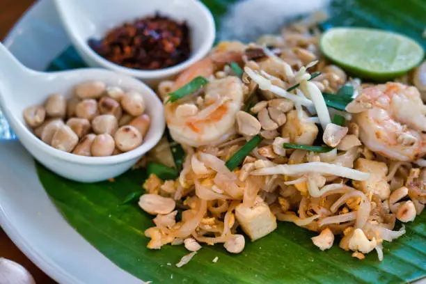 Close-up plate of traditional Thai Pad Thai fried tofu, noodles and Shrimp.  On the side a fresh slice of Lime with chilli and peanuts.