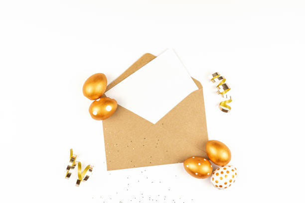 istock Easter festive decoration. Top view of easter eggs colored with golden paint and empty mock-up card in a kraft envelope. Various dotted designs. White background. 1300078060
