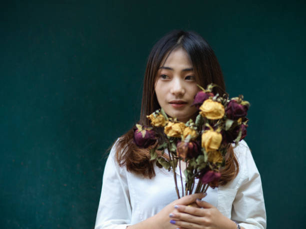 istock Female holding dried roses while standing in dark green background 1300078078