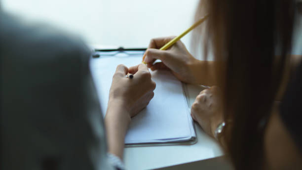 istock Two people hand writing on blank paper on clipboard while consulting on their work 1300078103