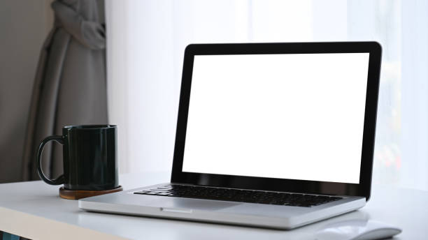 istock Mock up laptop computer with blank white screen and coffee cup on white table. 1300079924