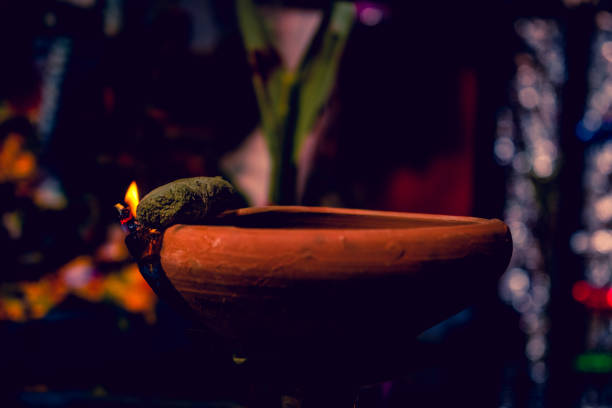 fotografia criativa de uma lâmpada de óleo de argila queimando realista em diwali, um festival indiano à noite. vermelho colorido, chama de fogo laranja amarelo aceso no fundo escuro da sombra noturna com efeito de grão de ruído. - gold bright brightly lit light - fotografias e filmes do acervo