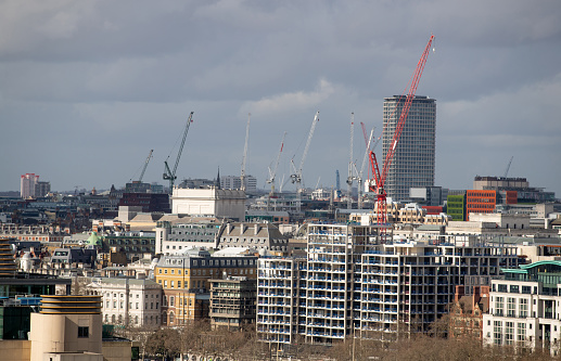 New construction in London downtown area, cranes rising over skyline towards gray cloudscape
