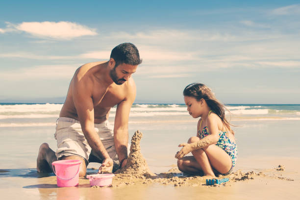 istock Focused handsome dad and little daughter building sandcastle 1300094055