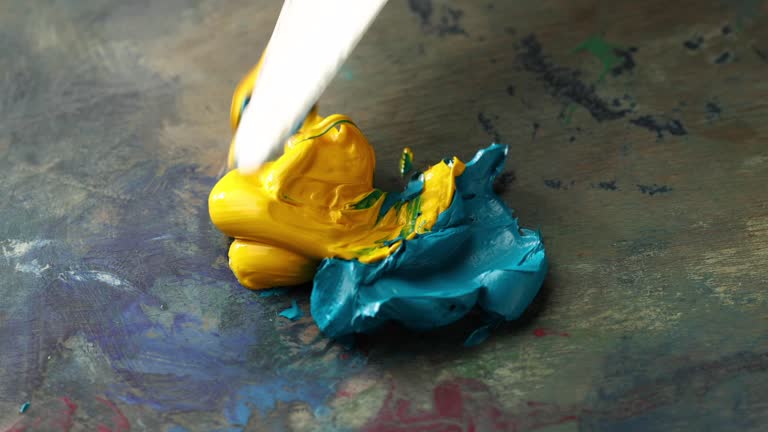 squeezes the oil paint out of the tube on artist palette and mixes the yellow and blue colors to form a green, close-up