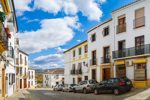 A small narrow street with white houses and cars in the old European city. Ronda, Andalusia, Spain. Panorama. 11 September 2019