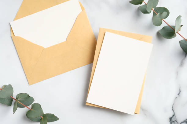 istock Craft paper envelopes with blank greeting cards mockups and eucalyptus leaves on marble table. Flat lay, top view. 1300098083