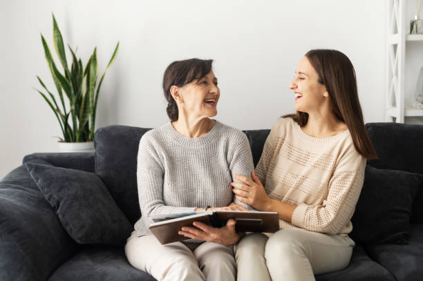 A senior mother and an adult daughter Two women diverse generations spend leisure time at home, a senior mother and an adult daughter is watching pictures in photo album together, remember pleasant moments. Family bonds family photos album stock pictures, royalty-free photos & images