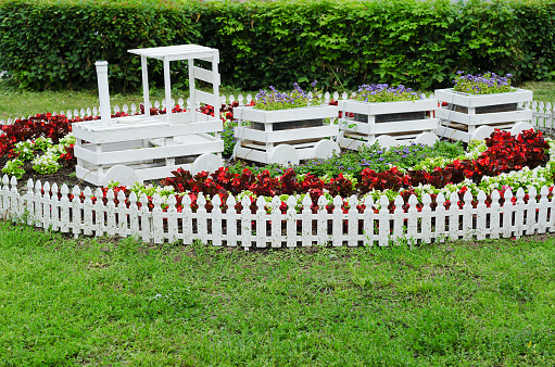 Creative flowerbed with flowers in the form of a train of boxes and a white fence, on a green lawn