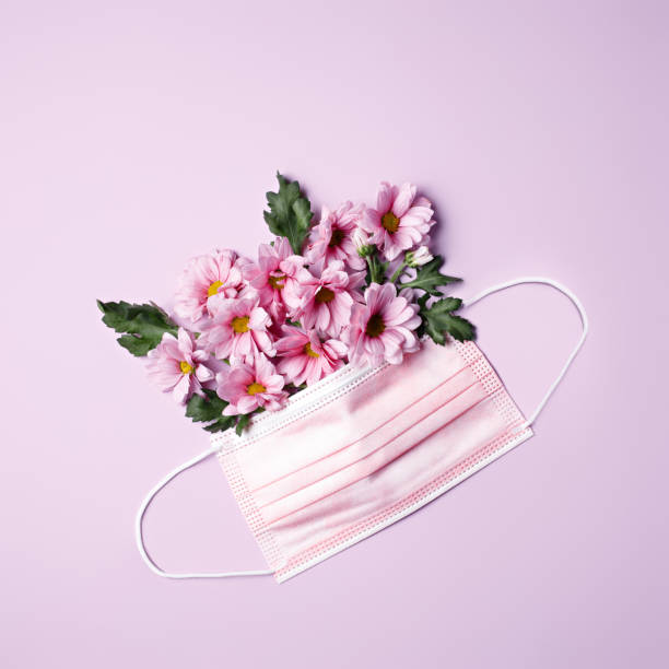 istock Protective surgical mask with arranged flowers on pastel lavender background 1300100537