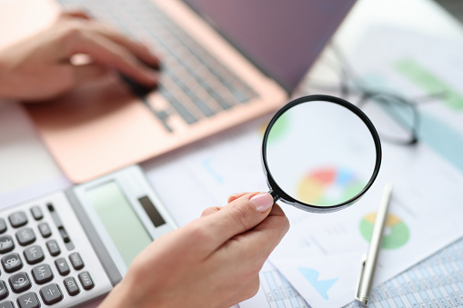 Female hands are typing on keyboard and holding magnifying glass closeup. Accounting department financial statement concept