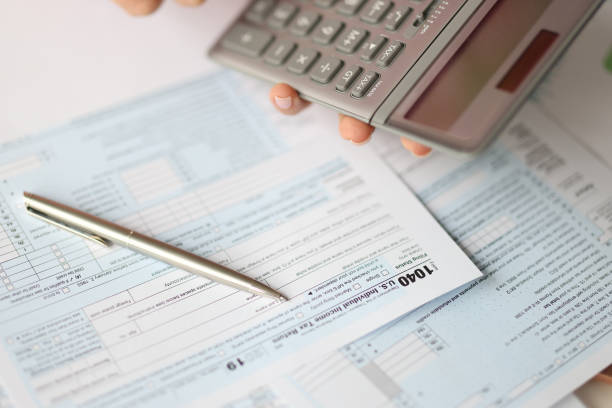 istock Hand holding calculator over tax form document closeup 1300104814