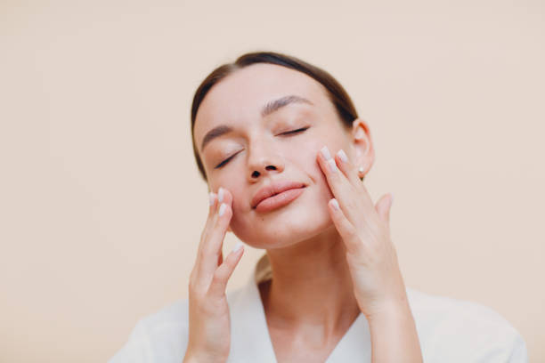 giovane donna che applica crema bianca cosmetica sul viso - modella per artisti foto e immagini stock