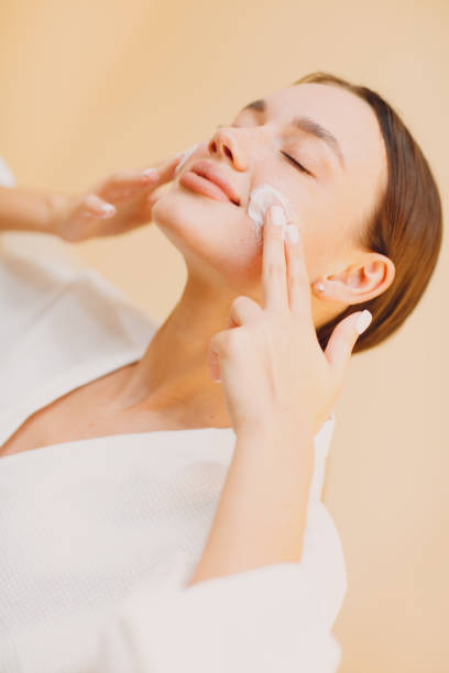 istock Young woman applying cosmetic white cream on her face 1300104972