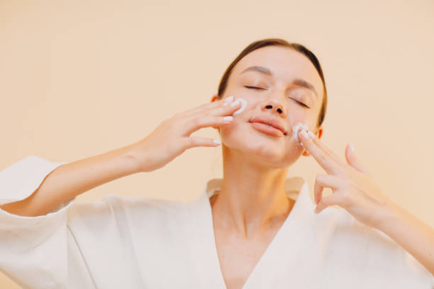 istock Young woman applying cosmetic white cream on her face 1300104977