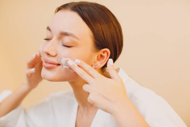 istock Young woman applying cosmetic white cream on her face 1300104978