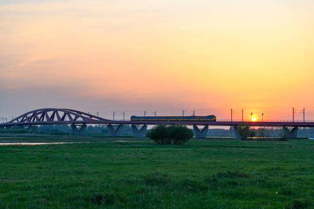 Dutch passenger train driving over the Hanzeboog bridge over the river IJssel near Zwolle on a beautiful springtime sunset.