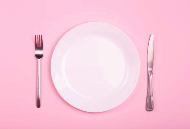 istock Empty plate on a pink background. White plate with knife and fork on a pink empty table 1300107806