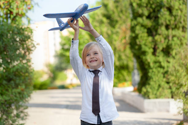 красивый мальчик с беззубой улыбкой в белой рубашке играет с игрушками самолета на открытом воздухе. - toothless smile фотографии стоковые фото и изображения