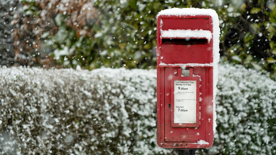 Red post box at Christmas covered with falling snow