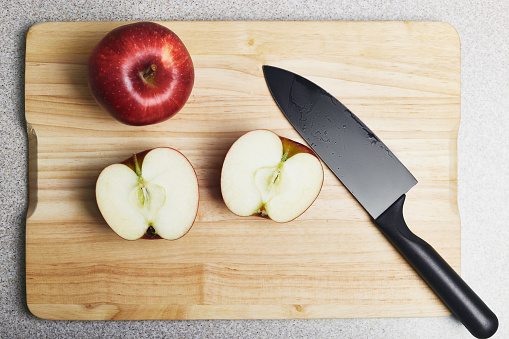 Cutting board with two red apples and a knife on it. One apple is whole, another one is cut, ready for cooking. Culinary class in a kitchen