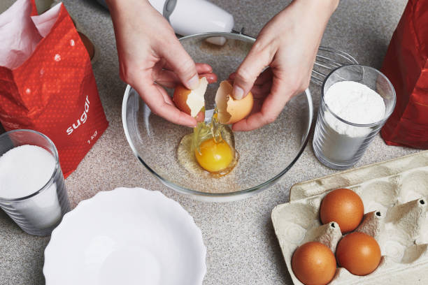 istock A Woman breaks an egg into transparent bowl. Ingredients for baking cake on a table. Cooking set. Tinted brown chicken eggs in a box, flour, pack of sugar, glasses, mixer. Culinary class in kitchen. 1300113555