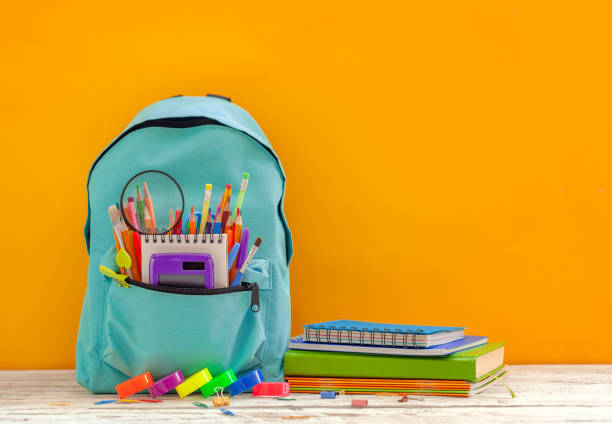 istock Full turquoise School Backpack with stationery on table on orange background. Back to school concept. 1300114974