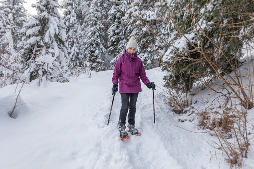 A snowy wintry scene of a woman snow shoeing up a mountain trail