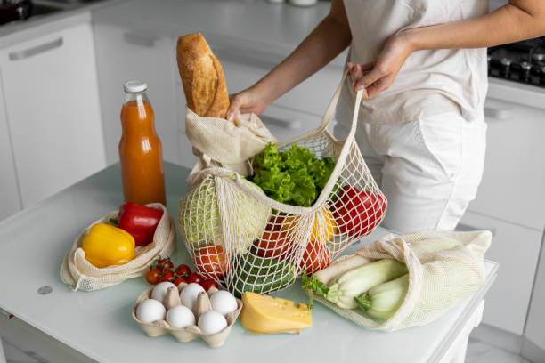 Woman came back from a market and unpacks a reusable grocery bag full of vegetables on a kitchen at home. Zero waste and plastic free concept. Girl is holding mesh cotton shopper with vegetables la mujer regresó de un mercado y desempaqueta una bolsa de comestibles reutilizable llena de verduras en una cocina en casa. concepto sin residuos cero y libre de plástico. chica está sosteniendo el comprador de algodón de malla con verduras.