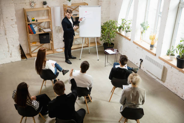istock Male speaker giving presentation in hall at workshop. Audience or conference hall. High angle of unrecognized participants. 1300116461