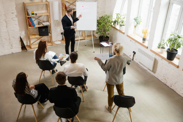 istock Male speaker giving presentation in hall at workshop. Audience or conference hall. High angle of unrecognized participants. 1300116469