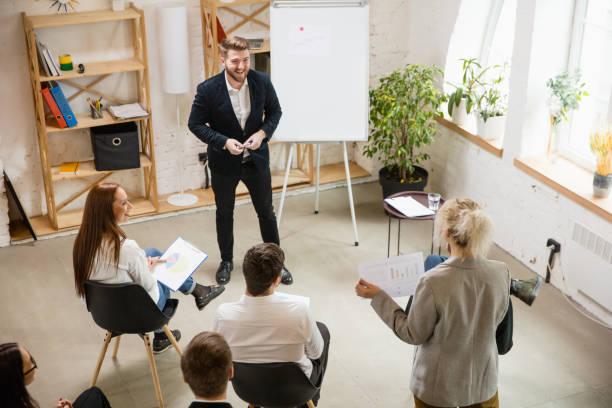 istock Male speaker giving presentation in hall at workshop. Audience or conference hall. High angle of unrecognized participants. 1300116470