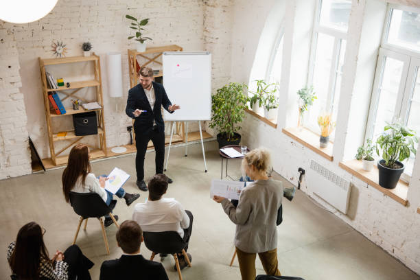 istock Male speaker giving presentation in hall at workshop. Audience or conference hall. High angle of unrecognized participants. 1300116472