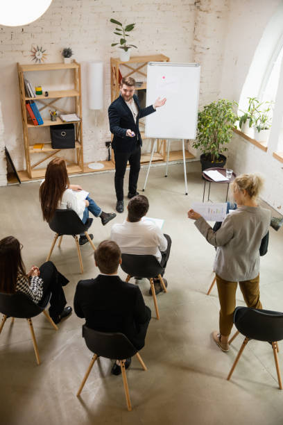 istock Male speaker giving presentation in hall at workshop. Audience or conference hall. High angle of unrecognized participants. 1300116474