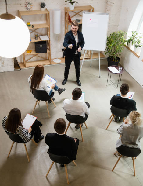 istock Male speaker giving presentation in hall at workshop. Audience or conference hall. High angle of unrecognized participants. 1300116477