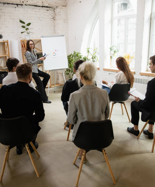 istock Female speaker giving presentation in hall at workshop. Audience or conference hall. Rear view of unrecognized participants. 1300116484
