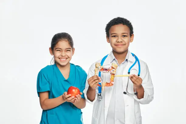 Photo of Fun multi-ethnic kids in medical uniforms are studying a human digestive system. Healthy food concept for children