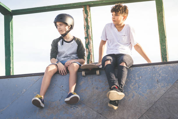 istock Low Angle View Of Boys Sitting On Wall Against Sky 1300121564