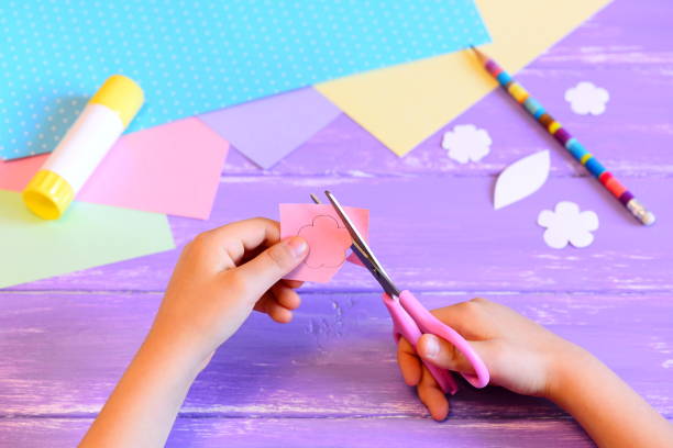 istock Small child creates a greeting card for mom. Step. Child holds scissors and cuts a flower from paper. Materials for creative art on a wooden table. Crafts idea for Mother's day or birthday or March 8 1300121769