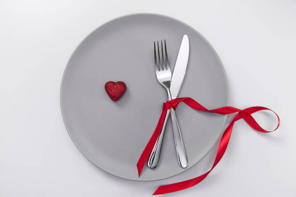 istock Valentine's day festive table setting, flat lay with red heart shape on gray plate, fork, knife and red ribbons on white table. Love dating concept. Place your text and copy space 1300121835